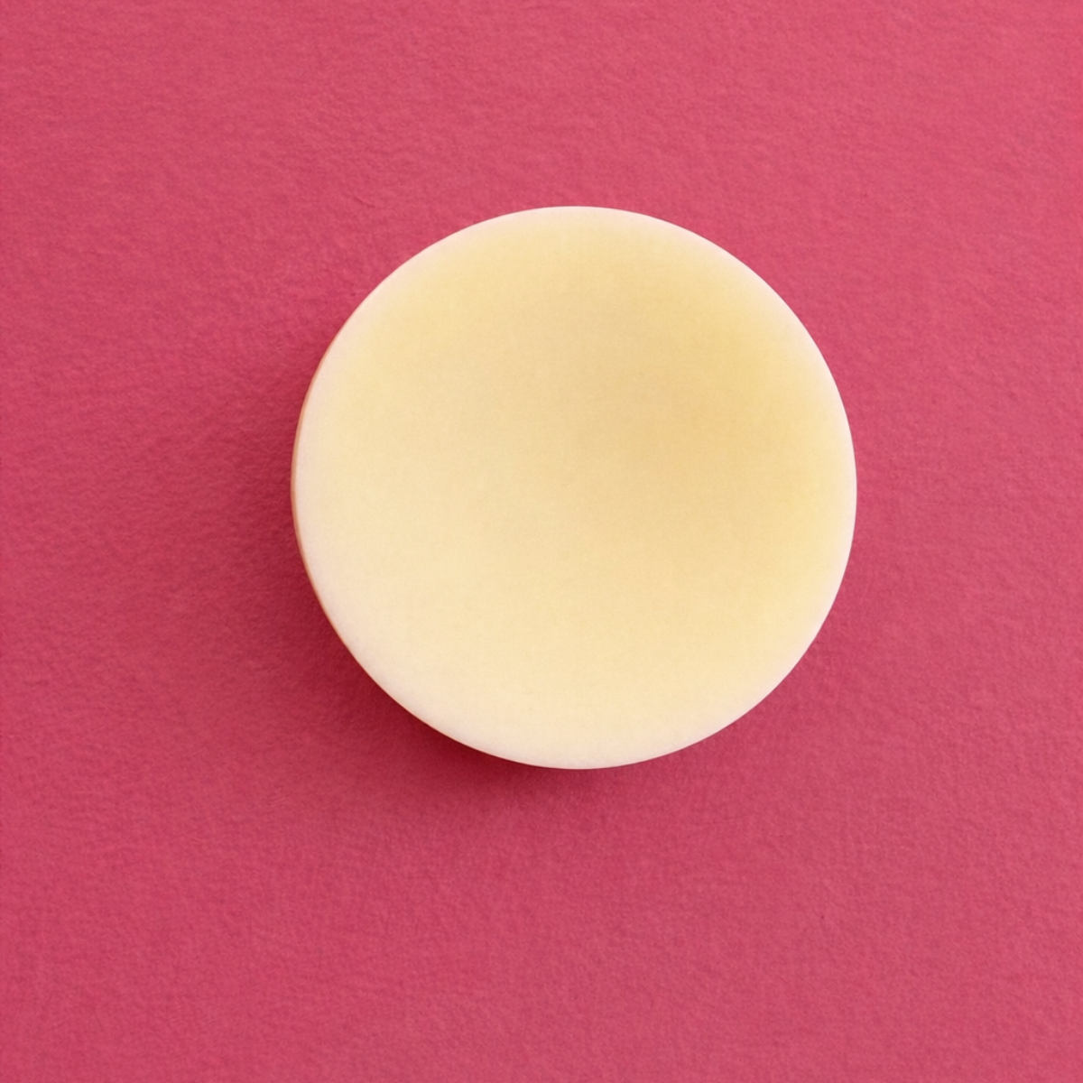 Round beige conditioner bar on a pink background